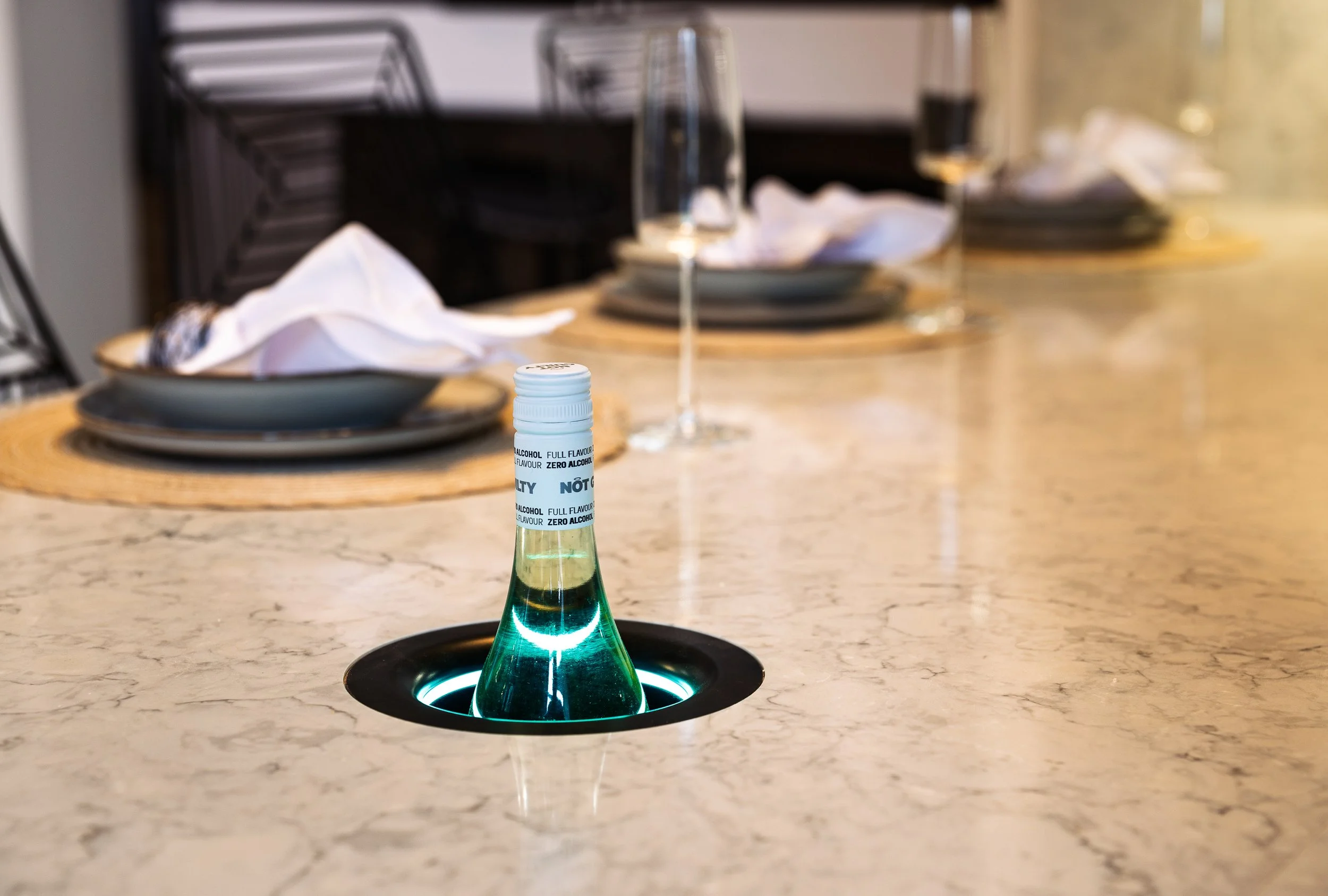 Close-up of the in-counter Kaelo Host drinks-cooler insert at Lion House: marble quartz worktop, glass with mineral water, two place settings behind, demonstrating worktop-integrated cooling installed by Oriel Kitchens